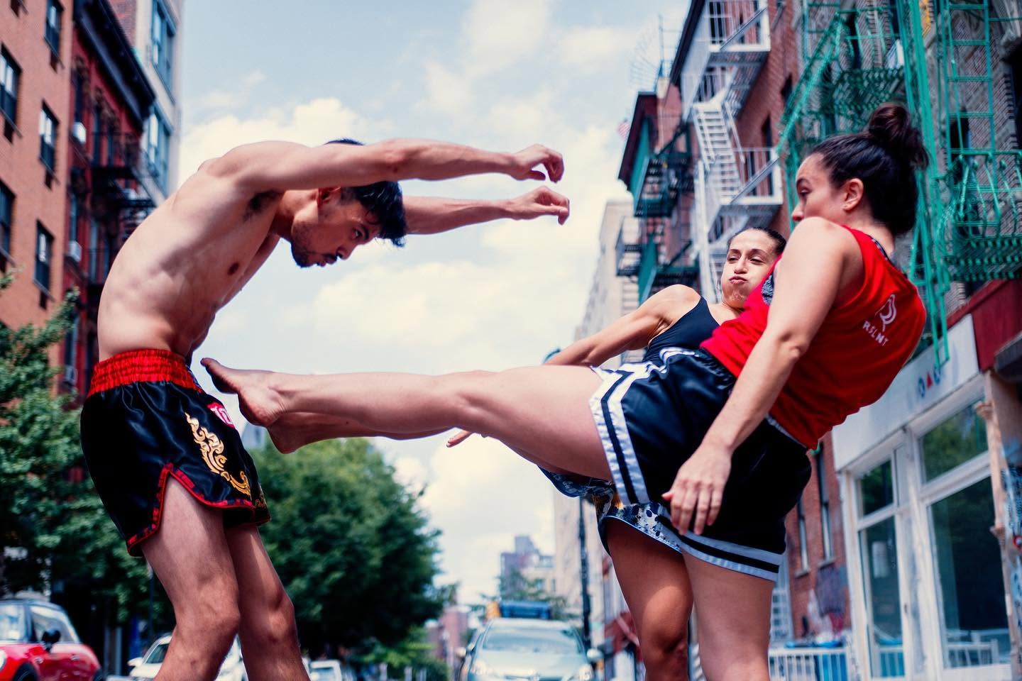 Two Muay Thai athletes demonstrate a kick on a New York City street while wearing RSLNT fightwear.