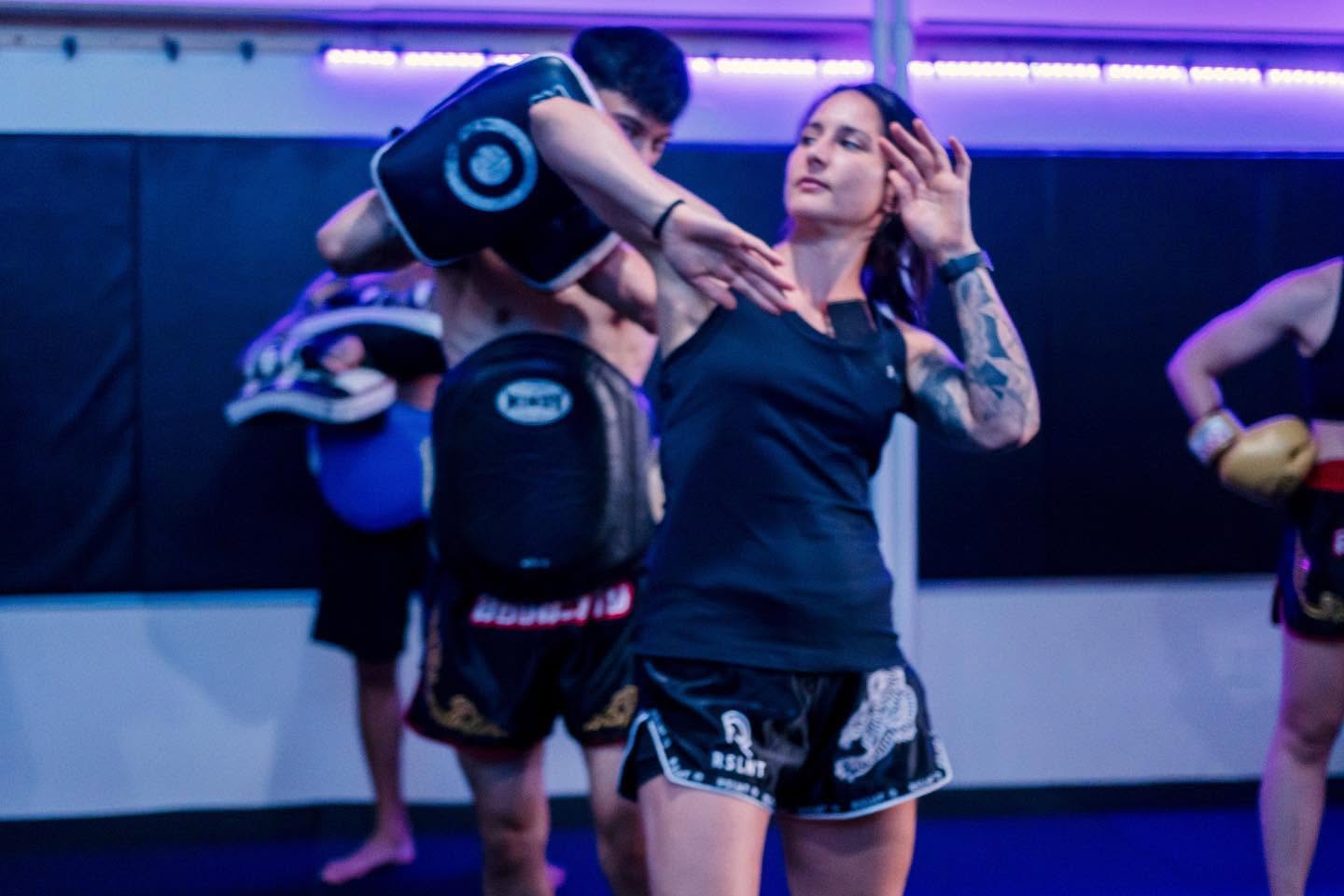 An athlete training with focus mitts while wearing RSLNT fightwear.