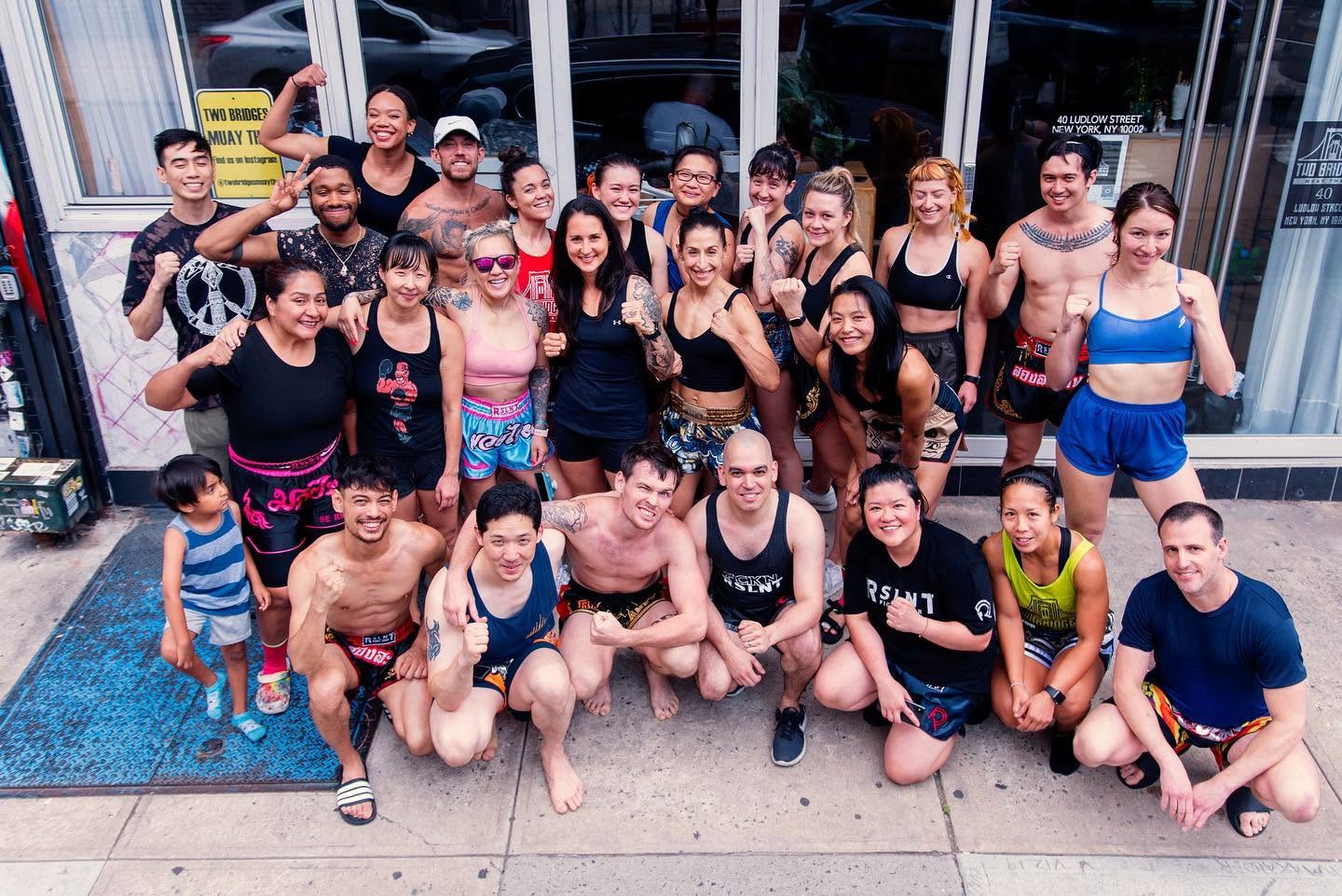 A diverse group of Muay Thai athletes and community members wearing RSLNT apparel outside Two Bridges Muay Thai.
