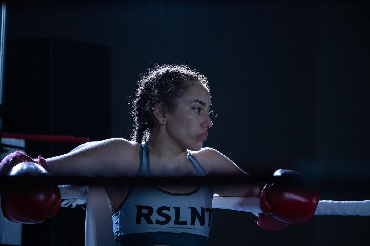 A boxer wearing RSLNT gear leaning against the ropes between rounds.