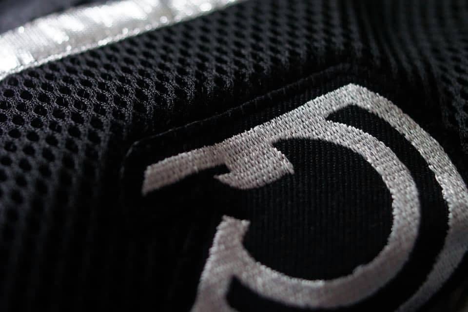 Close-up of the embroidered RSLNT monogram on technical black fabric.